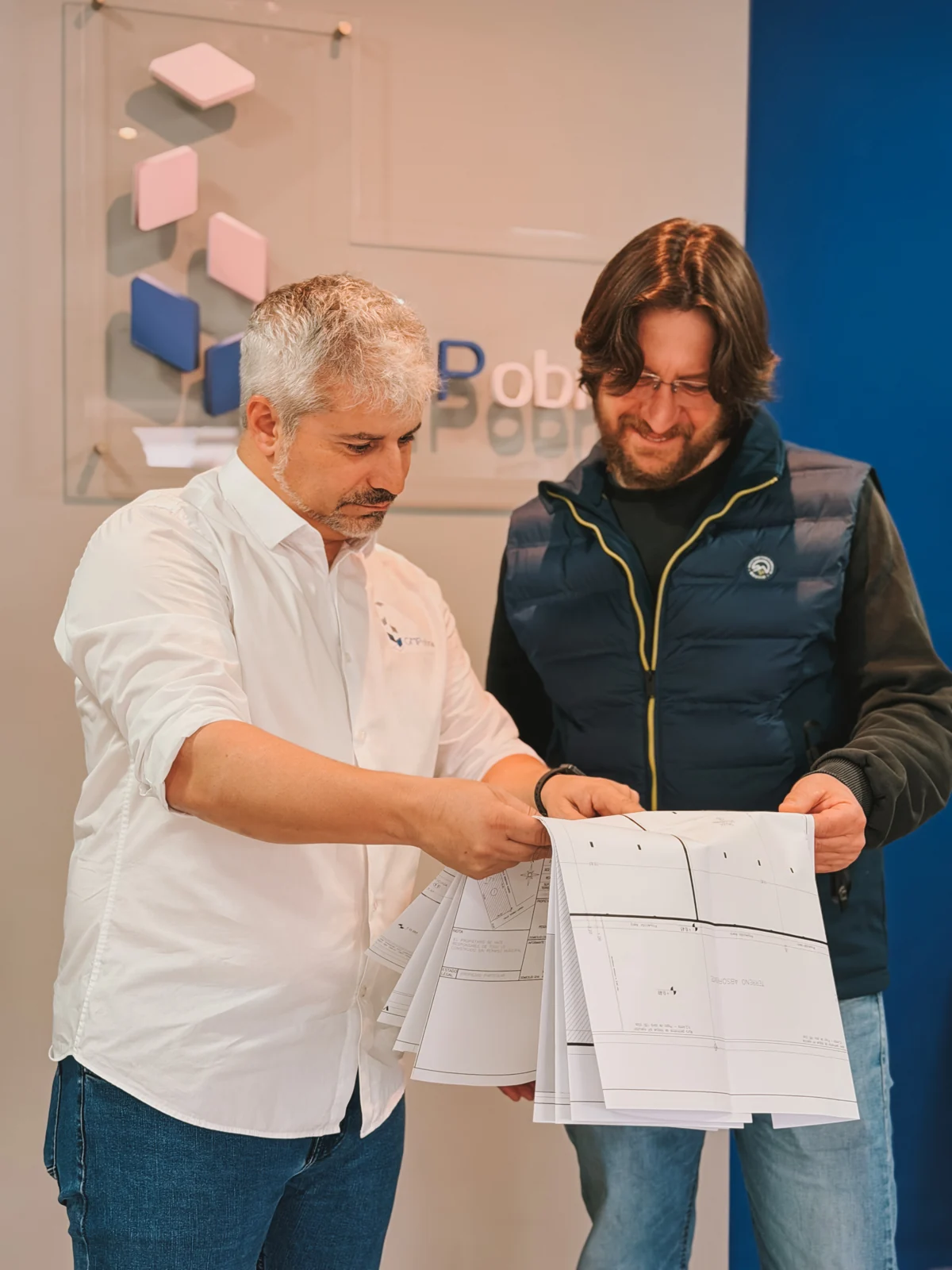 Gustavo Pinto señala un plano junto a otra persona en la oficina de GMP Obras.